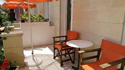 Ulkoiluterassi, jossa kaksi oranssista tuolia ja valkoinen pöytä varjon alla. (Tekoälyn luoma teksti)