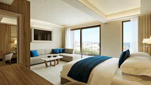 Moderni hotellihuone, jossa on parivuode, oleskelualue ja suuret ikkunat, joista on näkymä merelle. (Tekoälyn luoma teksti)