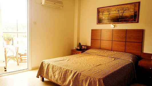 Makuuhuone, jossa on sänky, yöpöytä ja taulu seinällä; vieressä avoin parvekkeen ovi. (Tekoälyn luoma teksti)