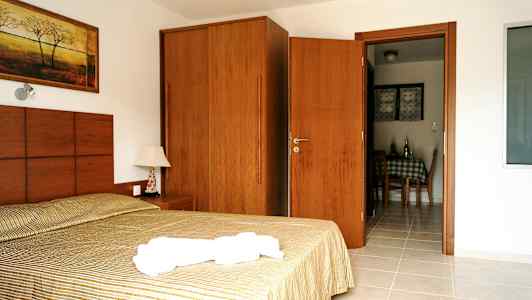 Kuva hotellihuoneesta, jossa on sänky, yöpöytä, kaappi ja ovi ruokailutilaan. (Tekoälyn luoma teksti)