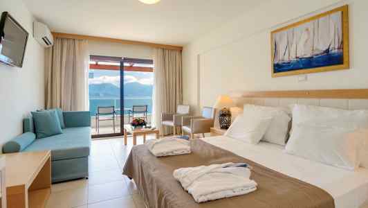 Hotellihuone, jossa on parivuode, sohva, pöytä kukilla ja merinäkymä lasiovien kautta. (Tekoälyn luoma teksti)