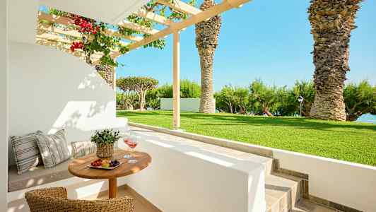 Ulkona ruokailualue, jossa pöytä ja tuolit puutarhassa palmujen ja merinäköalan äärellä. (Tekoälyn luoma teksti)