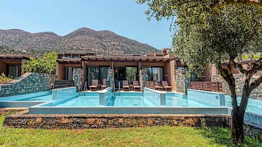 Yksityiset uima-allasalueet lomamökkien edessä, taustalla vuoria. (Tekoälyn luoma teksti)