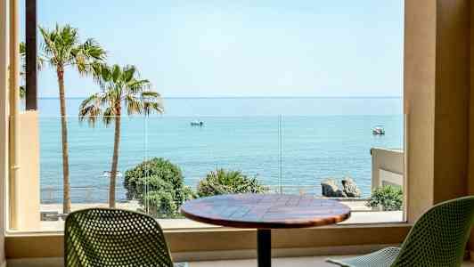 Näkymä huoneesta merelle, palmuja ja tuoleja terassilla. (Tekoälyn luoma teksti)