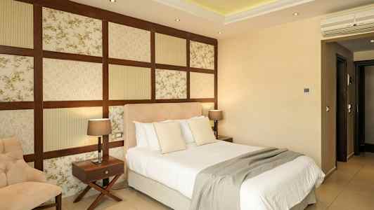 Hotellihuone, jossa on sänky, tuoli ja kaksi yöpöytää lampuilla. (Tekoälyn luoma teksti)