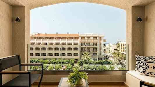 Näkymä hotellin parvekkeelta, jossa on sohvakalusteita, kasveja sekä rakennuksia ja puita taustalla. (Tekoälyn luoma teksti)