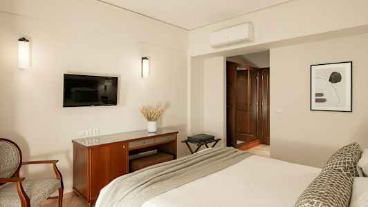 Kuva hotellihuoneesta, jossa on sänky, seinällä oleva televisio, kirjoituspöytä ja nojatuoli. (Tekoälyn luoma teksti)