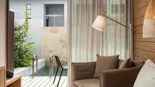 Huone, jossa on ruskea nojatuoli, lattiavalaisin ja näkymä terassille ja uima-altaalle. (Tekoälyn luoma teksti)