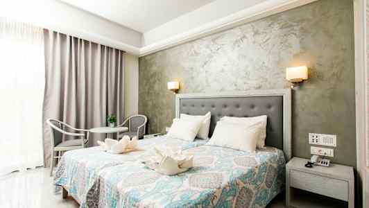 Hotellihuone, jossa on parivuode, yöpöytä, koristeellinen päiväpeite ja istuinryhmä. (Tekoälyn luoma teksti)