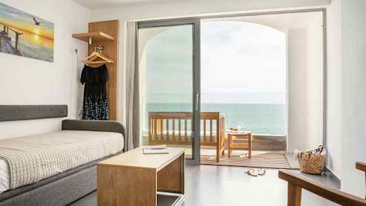 Hotellihuone, josta on merinäköala. Sänky ja sohvapöytä lasioven edessä, joka johtaa verannalle. (Tekoälyn luoma teksti)