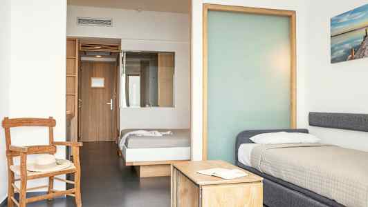 Hotellihuone, jossa kaksi sänkyä, tuoli ja pöytä. (Tekoälyn luoma teksti)