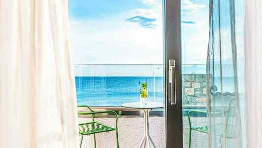Näköala huoneesta parvekkeelle, jossa pöytä ja tuolit, taustalla meri. (Tekoälyn luoma teksti)