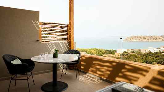 Terassi, jossa on pöytä, tuoleja ja näkymät merelle ja pienelle saarelle. (Tekoälyn luoma teksti)