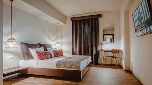 Hotellihuone, jossa on parivuode, kirjoituspöytä ja tuoli sekä televisio seinällä. (Tekoälyn luoma teksti)