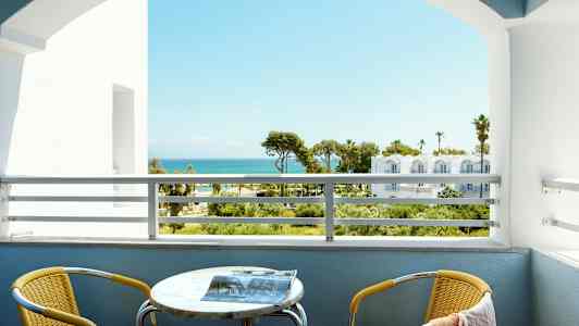 Näköala parvekkeelta merelle taustalla. Parvekkeella on keltainen tuoli ja pöytä. (Tekoälyn luoma teksti)