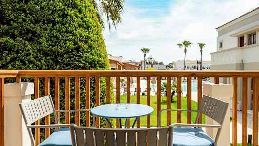 Näkymä parvekkeelta, jossa pöytä ja tuolit, kohti puutarhaa ja uima-allasta. (Tekoälyn luoma teksti)