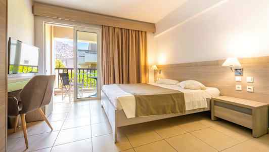 Hotellihuone, jossa on parivuode, työpöytä ja tuoli. Parvekkeen ovet johtavat parvekkeelle, josta on näkymät. (Tekoälyn luoma teksti)