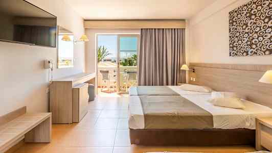 Hotellihuone, jossa on kaksi vuodetta, kirjoituspöytä, televisio ja avautuva ovi parvekkeelle. (Tekoälyn luoma teksti)