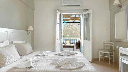 Hotellihuone, jossa on sänky, tuolit ja pöytä sekä näkymä ovien kautta parvekkeelle ja taustalla oleville vuorille. (Tekoälyn luoma teksti)