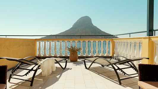 Terassi aurinkotuoleilla ja näkymä merelle sekä pienelle vuorimuodostumalle. (Tekoälyn luoma teksti)