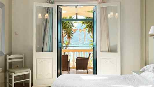 Vaalea makuuhuone, jonka avautuvat ovet johtavat parvekkeelle, jossa on huonekaluja ja näkymä merelle. (Tekoälyn luoma teksti)