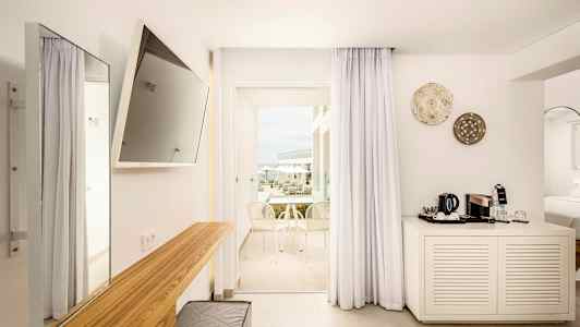 Moderni hotellihuone, jossa on vaalea sisustus, seinällä televisio, työpöytä ja parveke näkymällä. (Tekoälyn luoma teksti)