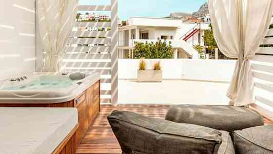 Kuvassa näkyy terassi, jossa on poreallas, aurinkotuolit ja näkymä naapurirakennukseen. (Tekoälyn luoma teksti)