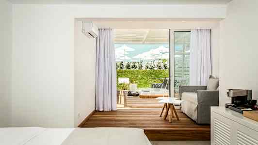 Hotellihuone, jossa on moderni makuuhuone, istuinalue ja ulkoterassi, nurmikko ja aurinkotuolit. (Tekoälyn luoma teksti)