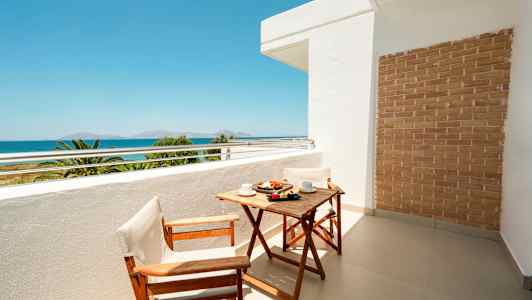 Parveke, jossa puupöytä ja kaksi tuolia, merinäköala taustalla. (Tekoälyn luoma teksti)