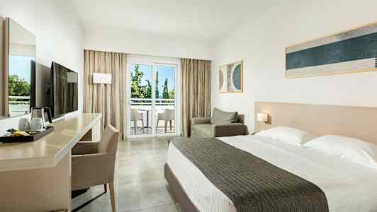 Hotellihuone, jossa parivuode, työpöytä ja tuoli, nojatuoli sekä parveke, jolta näkymä puihin. (Tekoälyn luoma teksti)