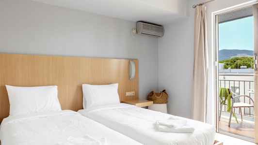 Hotellihuone, jossa on kaksi erillistä vuodetta, korilaukku ja parveke näkymillä. (Tekoälyn luoma teksti)