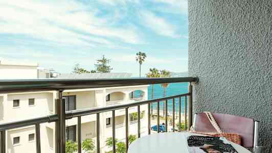 Näkymä parvekkeelta rannalle, taustalla meri ja palmuja. (Tekoälyn luoma teksti)