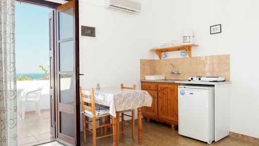 Pieni keittotila, jossa pöytä, tuolit ja keittoalue. Ovi johtaa parvekkeelle, josta on näkymä. (Tekoälyn luoma teksti)