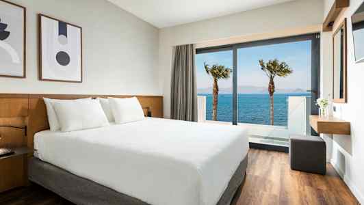 Hotellihuone, jossa valkoinen sänky ja näkymä merelle lasioven läpi. (Tekoälyn luoma teksti)