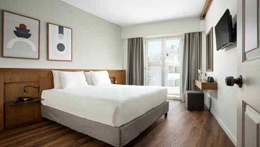 Moderni hotellihuone, jossa on parivuode, taidetta seinällä ja parveke lasiovella. (Tekoälyn luoma teksti)