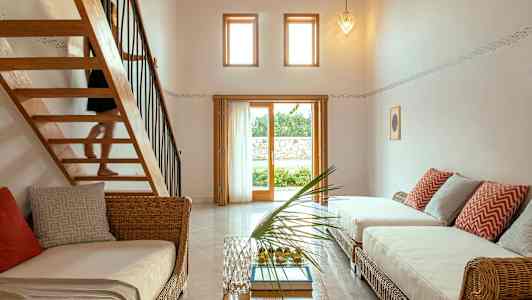 Valoisa huone, jossa rottinkihuonekaluja, suuret ikkunat ja portaat yläkertaan. (Tekoälyn luoma teksti)