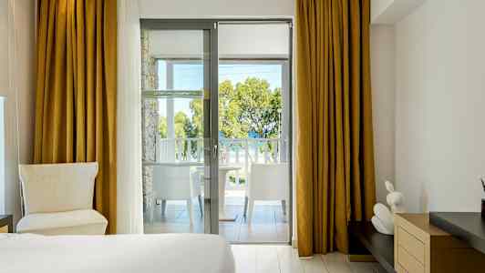 Hotellihuone, jolta on näkyvät parvekkeen kautta puihin ja mereen. (Tekoälyn luoma teksti)