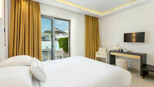 Hotellihuone valkoisilla kalusteilla, parisänky, kirjoituspöytä ja uloskäynti terassille. (Tekoälyn luoma teksti)