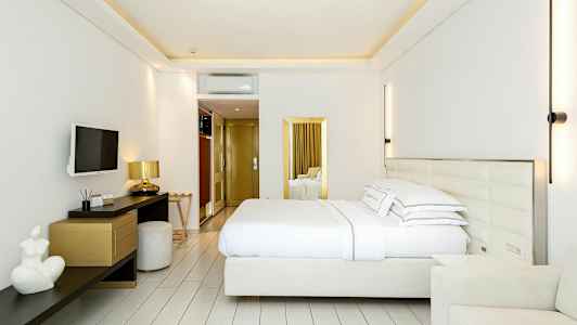 Moderni hotellihuone, jossa on parivuode, seinälle asennettu televisio, työpöytä ja tuoleja. (Tekoälyn luoma teksti)