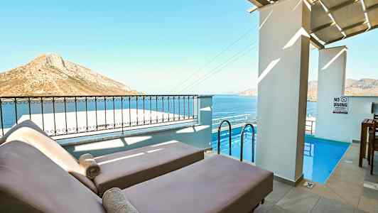 Kaksi aurinkotuolia pienen altaan äärellä, taustalla meri ja vuoristomaisema. (Tekoälyn luoma teksti)