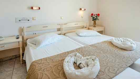 Hotellihuone, jossa on kaksi yhden hengen vuodetta, koriste-esineitä ja kukkavaasi yöpöydällä. (Tekoälyn luoma teksti)