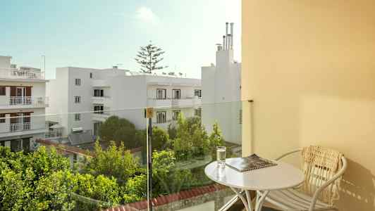 Parveke, jossa pöytä ja tuoli, näkymä valkoisiin rakennuksiin ja vehreyteen. (Tekoälyn luoma teksti)