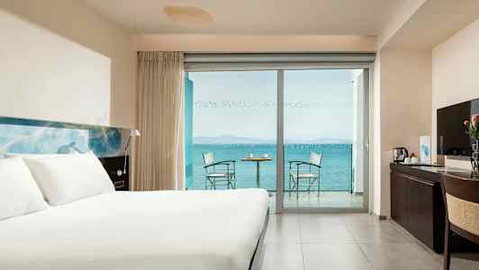 Hotellihuone, jossa on iso sänky, työpöytä ja parveke merinäköalalla. (Tekoälyn luoma teksti)