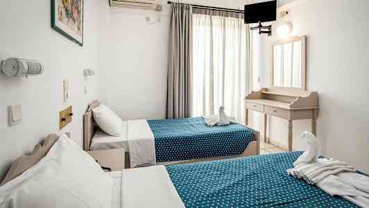 Kaksi yhden hengen vuodetta, joissa on sinipilkulliset päälliset, vaaleasti sisustetussa hotellihuoneessa. (Tekoälyn luoma teksti)