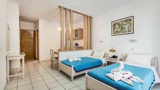 Hotellihuone, jossa on kaksi yhden hengen sänkyä, siniset päiväpeitteet ja koristellut pyyhkeet. (Tekoälyn luoma teksti)