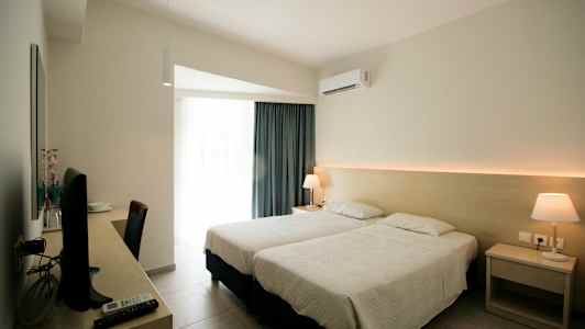 Hotellihuone, jossa kaksi erillistä vuodetta, kirjoituspöytä televisiolla ja yöpöydällä lamppu. (Tekoälyn luoma teksti)