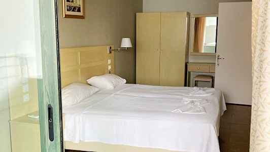 Kuva hotellihuoneesta, jossa on kaksi erillistä vuodetta valkoisilla vuodevaatteilla, vaatekaappi ja peili. (Tekoälyn luoma teksti)