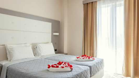 Hotellihuone, jossa on kaksi yhden hengen vuodetta koristeltu punaisilla ruusun terälehdillä. (Tekoälyn luoma teksti)