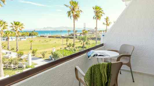 Parveke, jossa pöytä, tuolit ja näkymä vehreään puutarhaan palmuineen sekä mereen taustalla. (Tekoälyn luoma teksti)