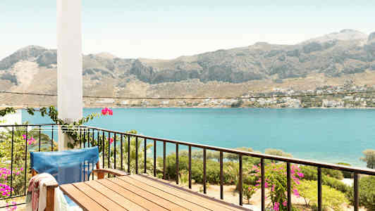 Parveke, jolla on pöytä ja tuoli, näkymä merelle ja vuorille taustalla. (Tekoälyn luoma teksti)